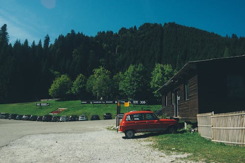 Red 5-door Hatchback Near the Brown Wooden House in Daytime