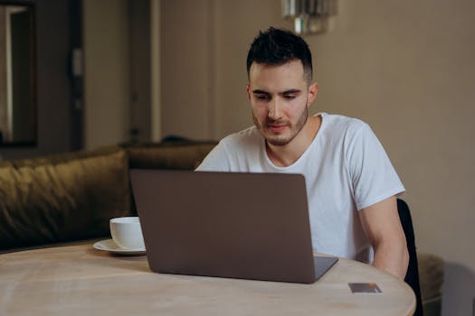 Young man concentrating on laptop in cozy home setting. Perfect for remote work or freelance visuals.