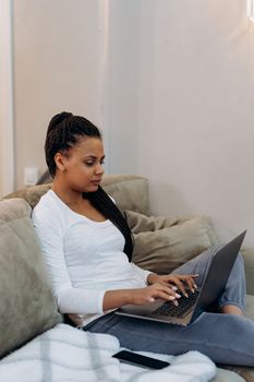 Woman sitting on a couch using a laptop, epitomizing modern digital nomad lifestyle.