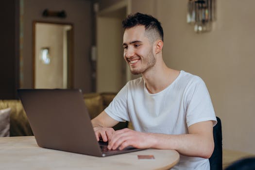 Young man smiling while online shopping with laptop indoors at home.