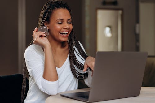 Happy Woman Holding her Credit while Looking at the Laptop 