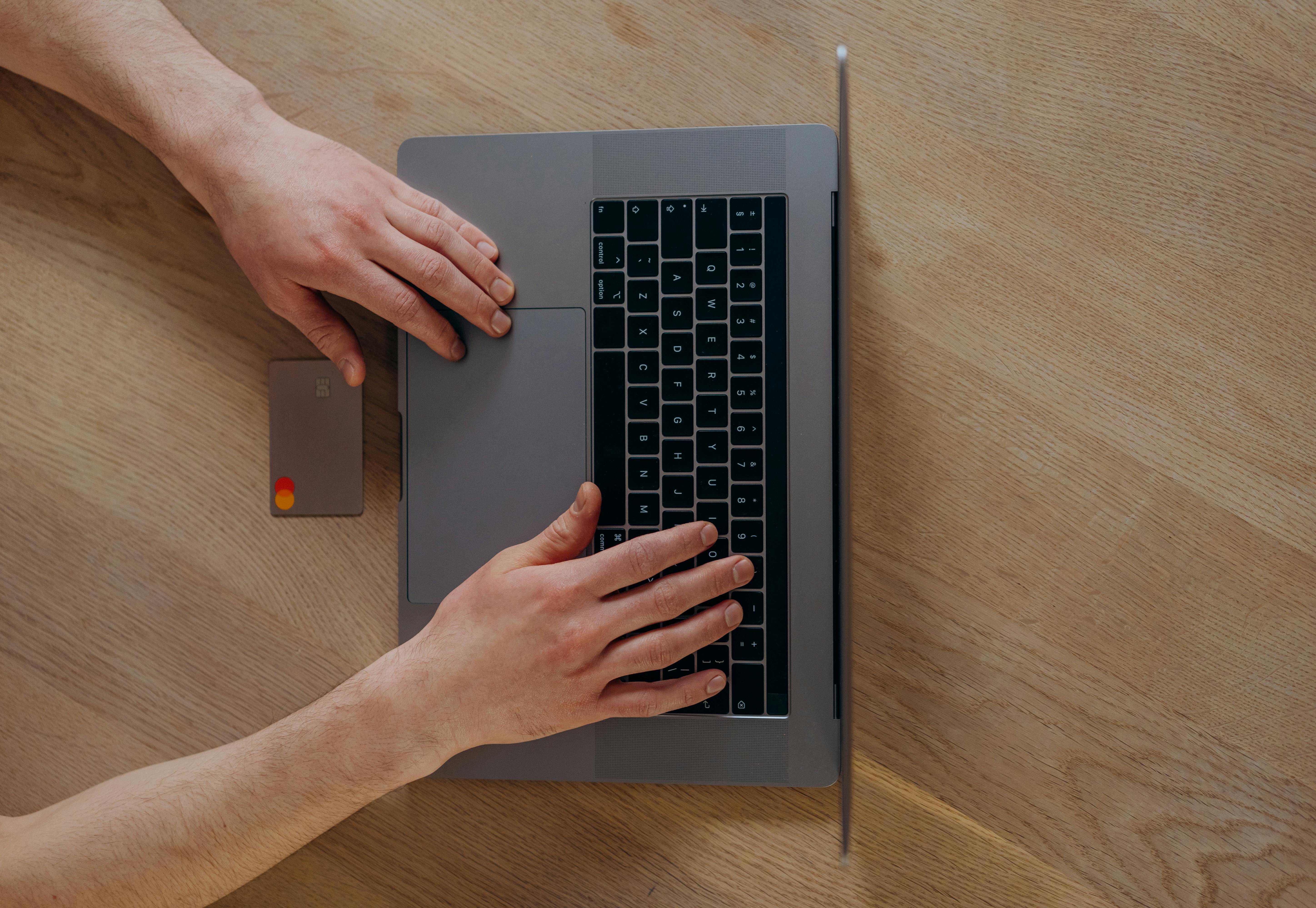 a person using a laptop beside a credit card on a wooden table