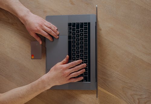 A Person Using a Laptop Beside a Credit Card on a Wooden Table