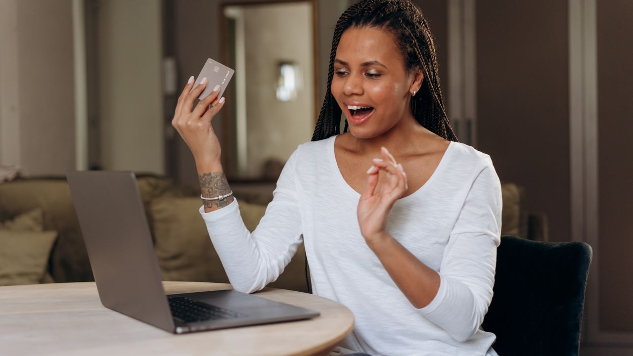 African American woman happily shopping online with a laptop and credit card.