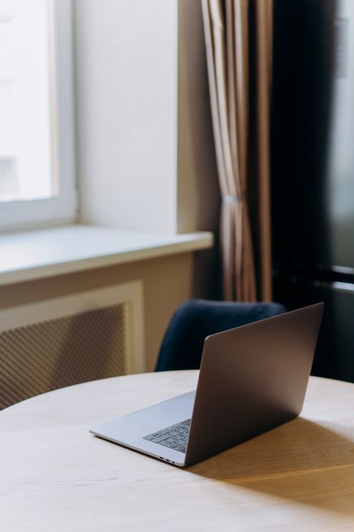 Free A sleek laptop sitting on a round wooden table in a bright, indoor setting. Stock Photo