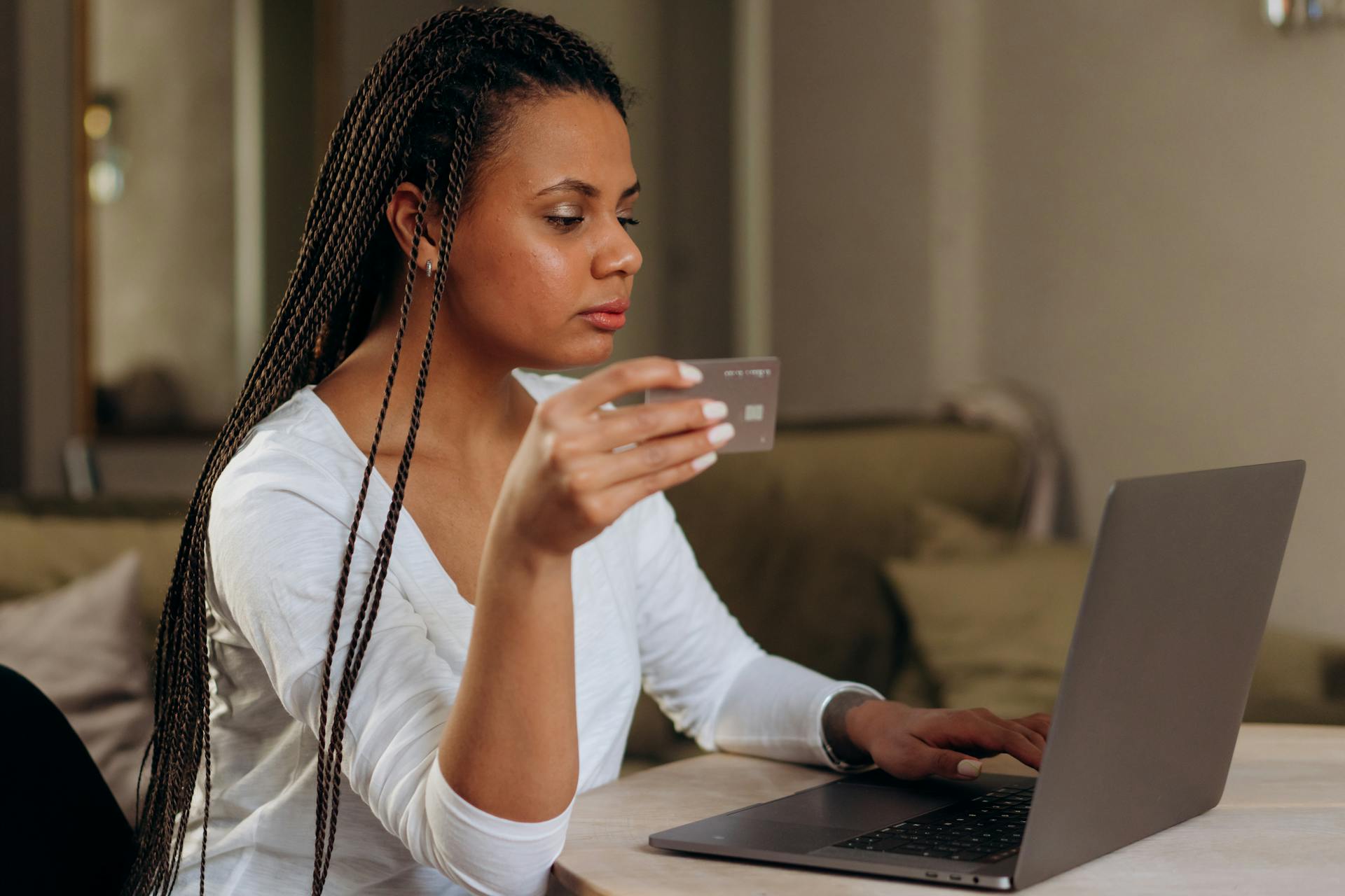 A woman with braided hair makes an online transaction using a credit card and laptop at home.