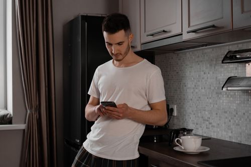 Free Adult male checking smartphone in stylish kitchen setting. Indoor scene. Stock Photo