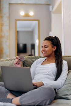 Black woman with braided hair using credit card for online shopping at home.