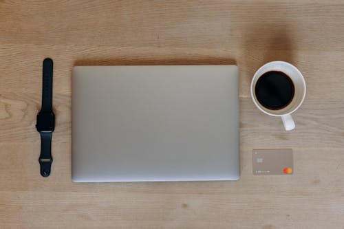 Close-Up Shot of a Laptop beside a Cup of Black Coffee and a Smartwatch on a Wooden Table
