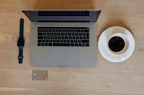 Close-Up Shot of a Laptop beside a Cup of Black Coffee and a Smartwatch on a Wooden Table