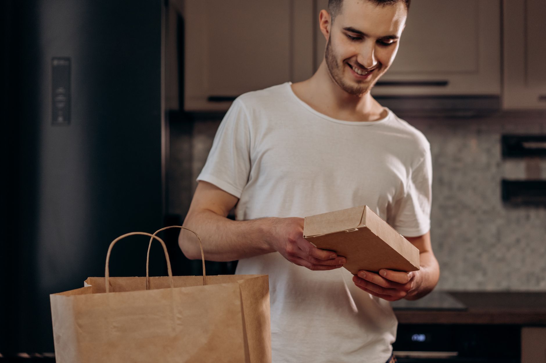 A man happily unpacks a food delivery in a modern kitchen setting.