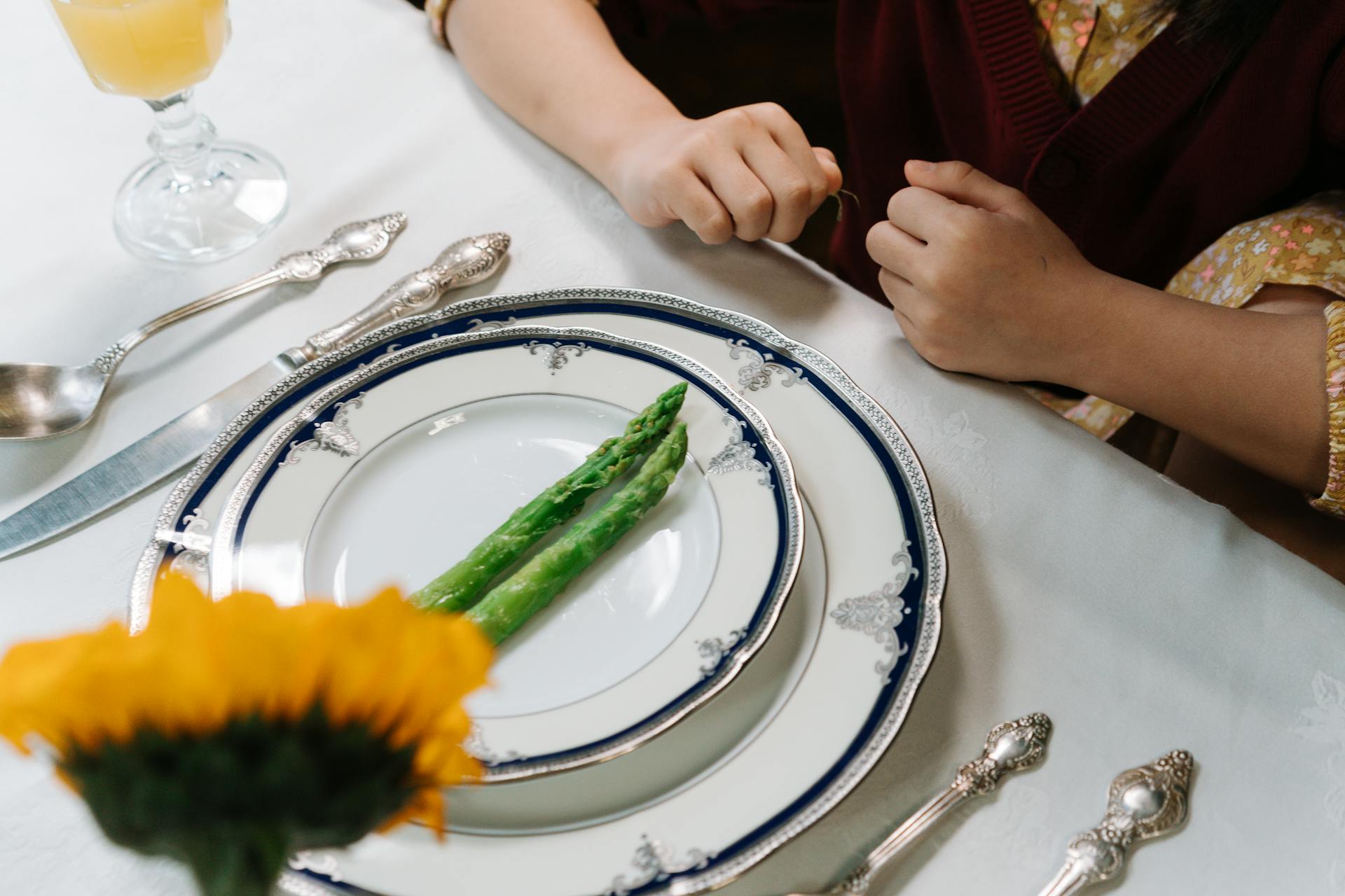 Elegant dinner setting with asparagus on fine china and silver cutlery on white tablecloth.