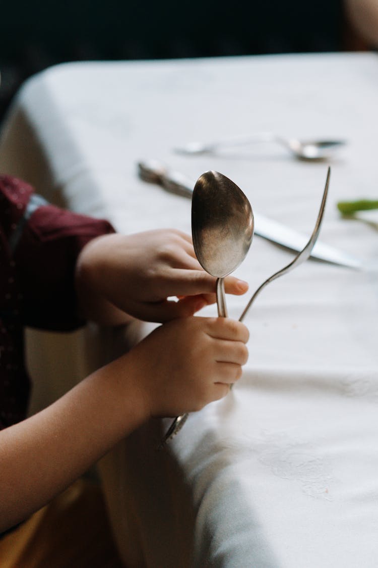 A Kid Holding A Silver Fork And Spoon