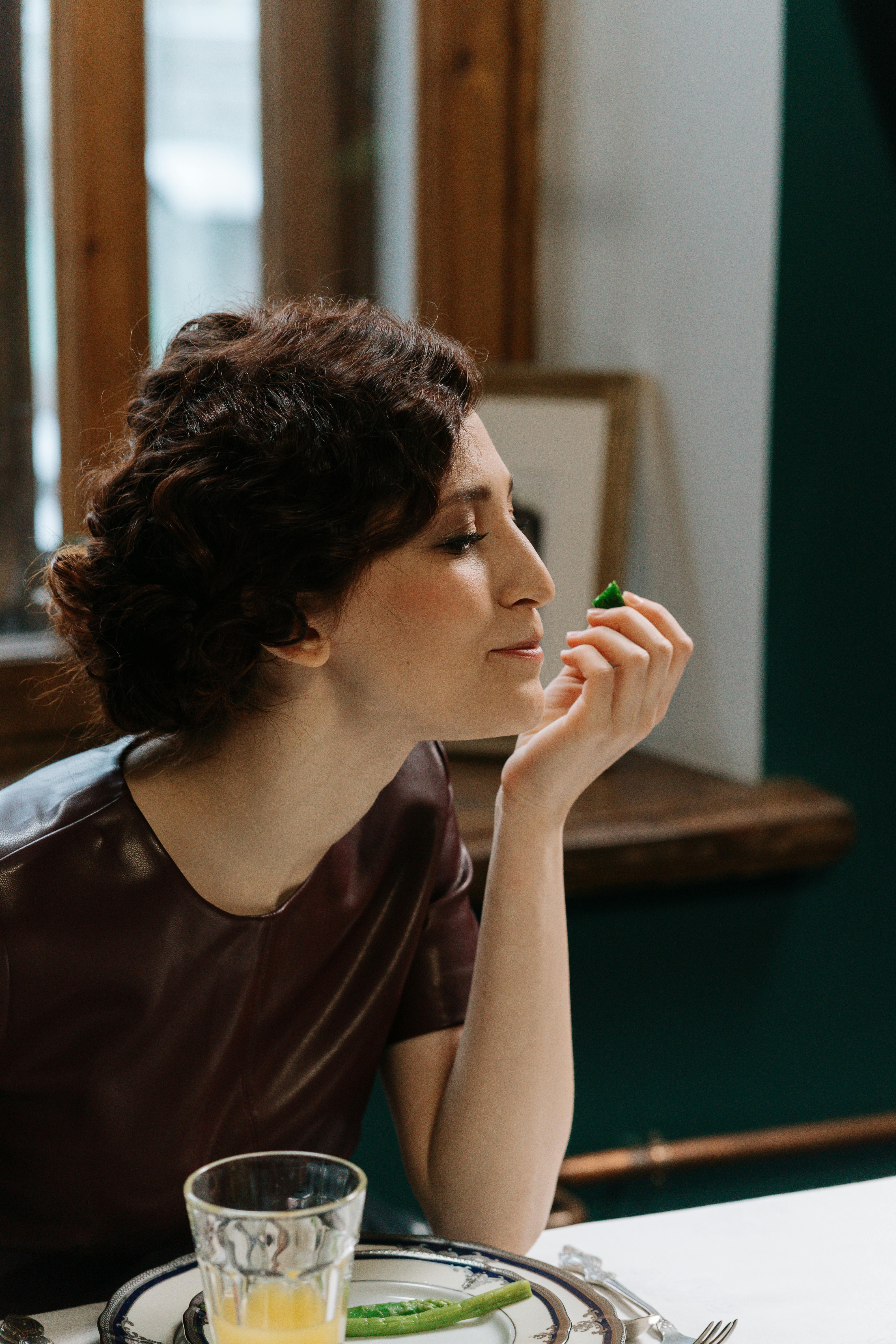 A woman in a maroon dress savoring a meal in a cozy, well-lit indoor setting.