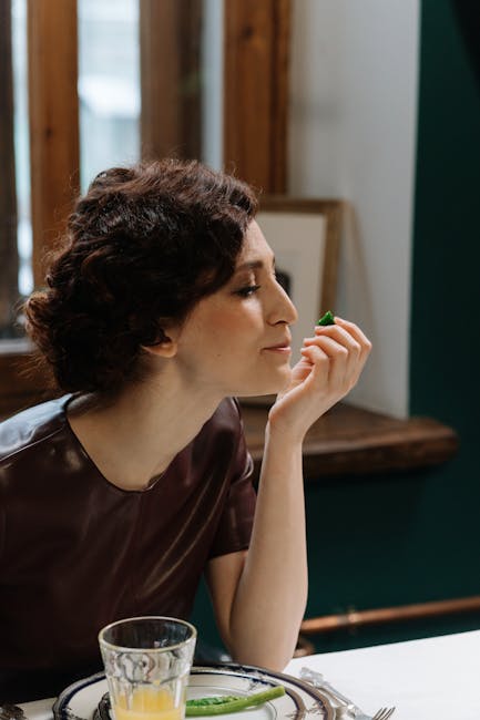 A woman in a maroon dress savoring a meal in a cozy, well-lit indoor setting.