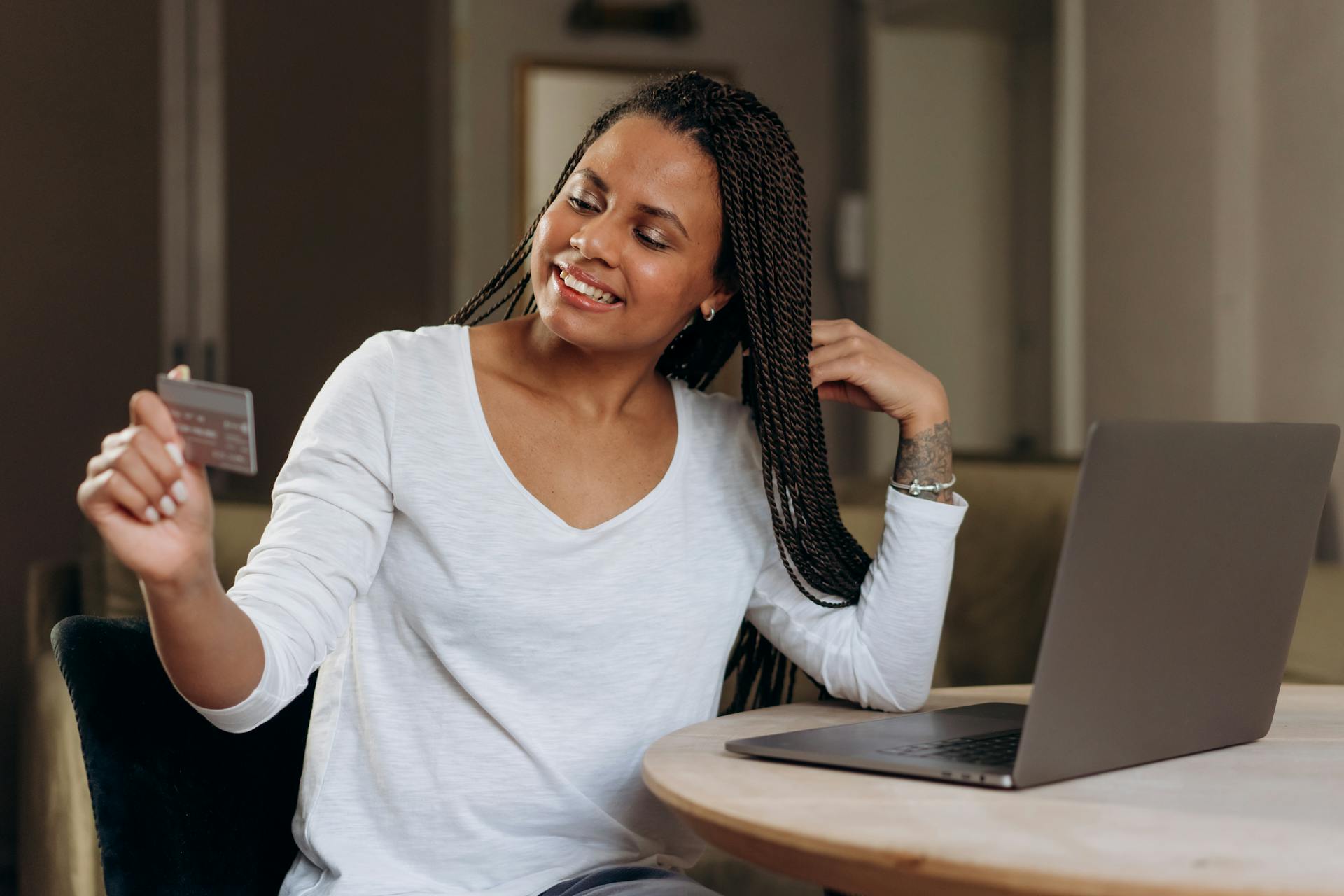 A smiling woman uses her credit card for an online transaction at home, embracing modern e-commerce convenience.