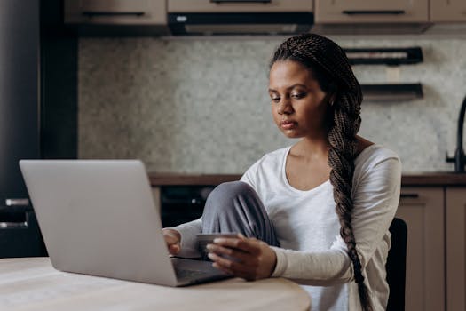 Young woman with braids using laptop and credit card for online shopping indoors.