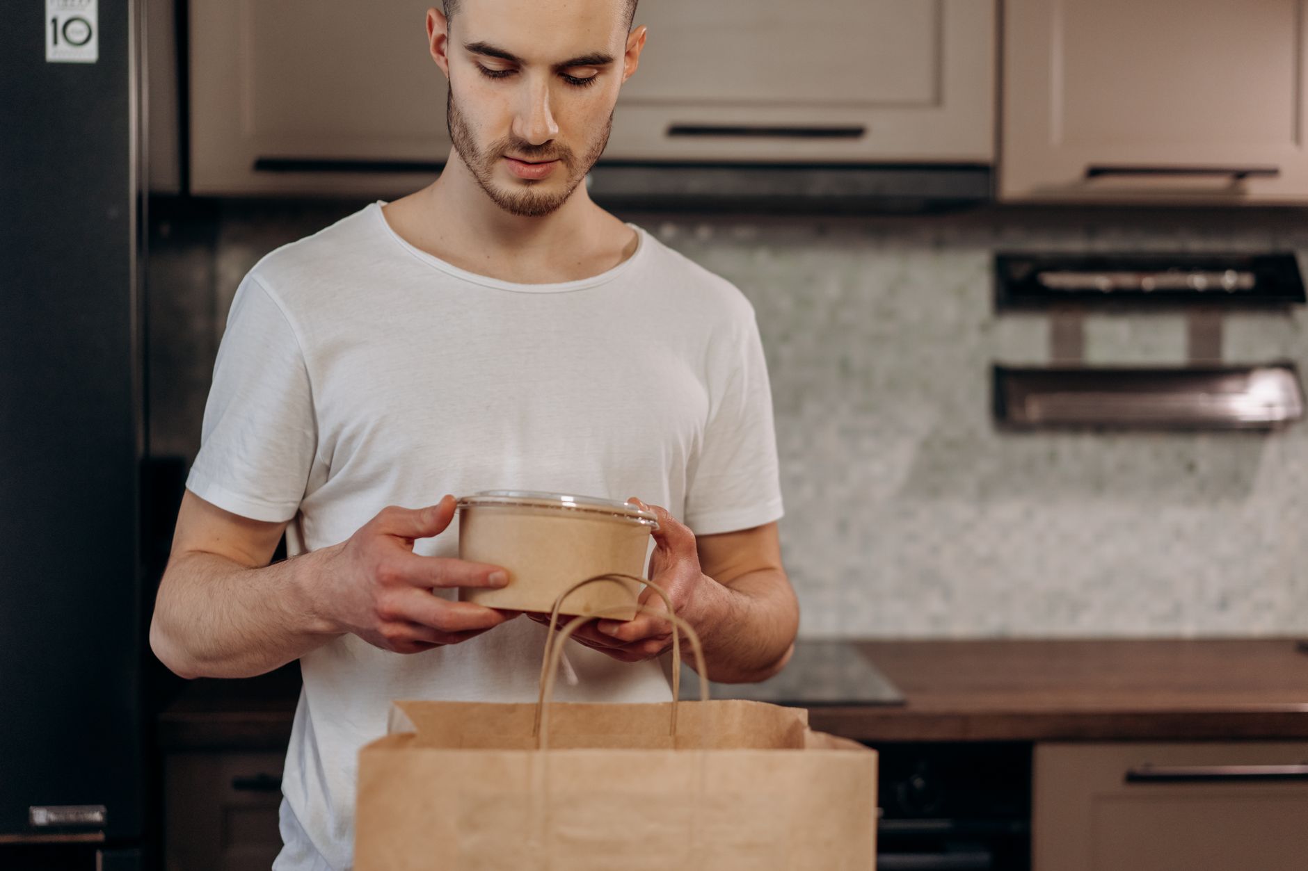 Adult man in a kitchen unpacking food delivery from a paper bag, showcasing eco-friendly packaging.