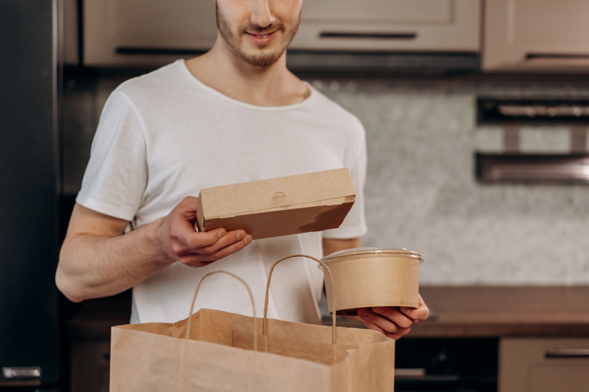 A man in a white shirt manages takeaway food in a kitchen, emphasizing convenience and modern lifestyle.