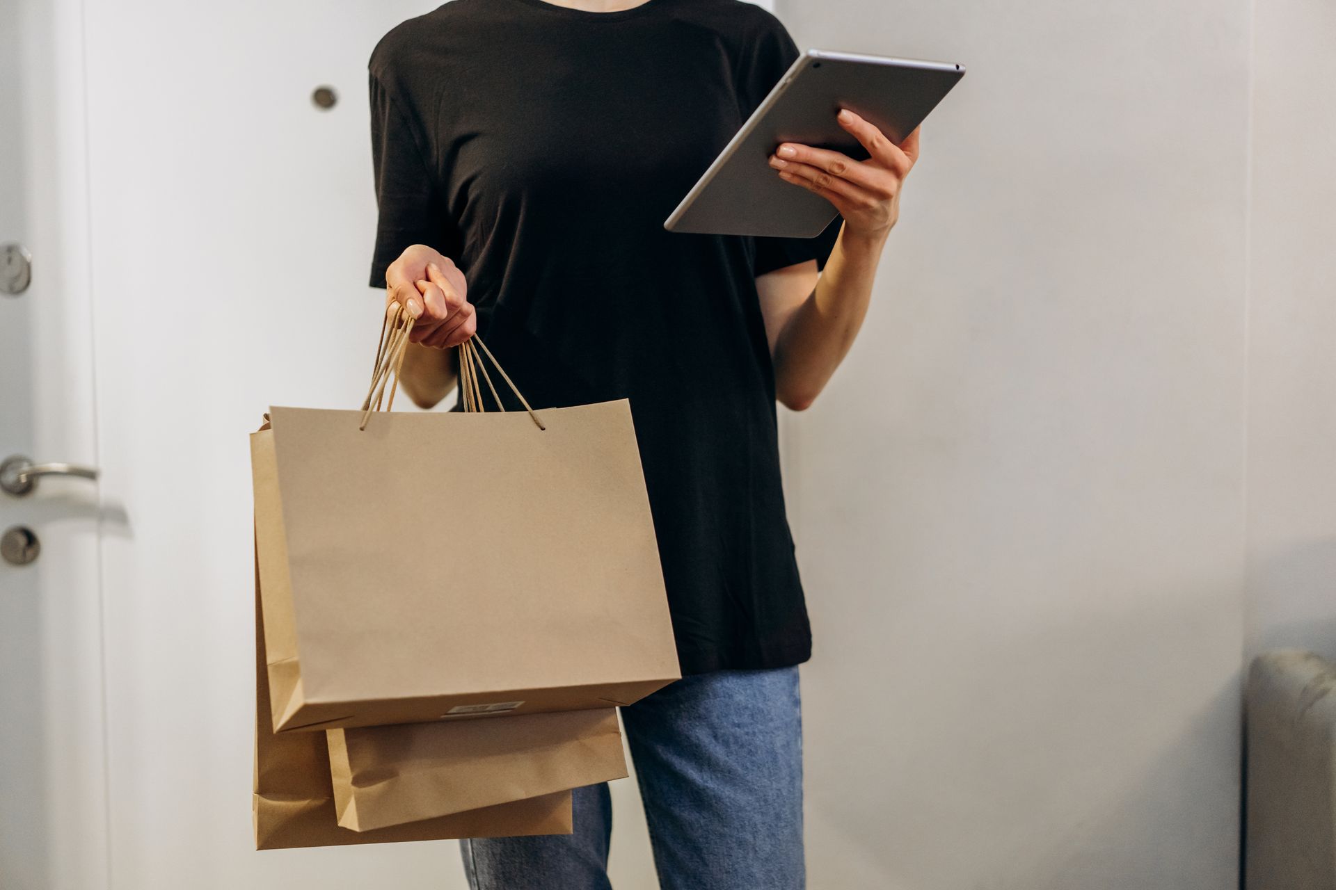 Woman in black shirt with shopping bags using a tablet at home, symbolizing online shopping convenience.