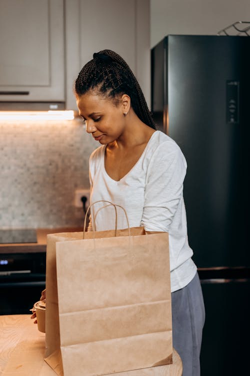 Woman in White Long Sleeve Shirt Standing beside Brown Paper Bag