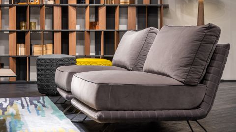 Interior design of modern living room furnished with comfortable settee with poufs against bookcase and shining lamp