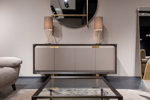 Glass table placed against stylish cupboard with decorative shining lamps under mirror in stylish apartment