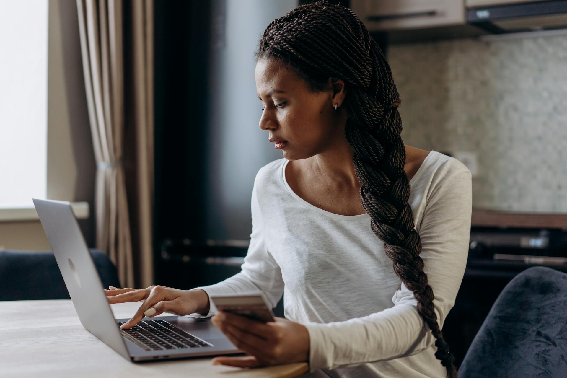 Young African American woman with braided hair making an online payment using laptop and credit card.