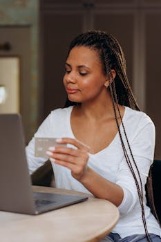 A woman doing online shopping using a laptop and credit card indoors.