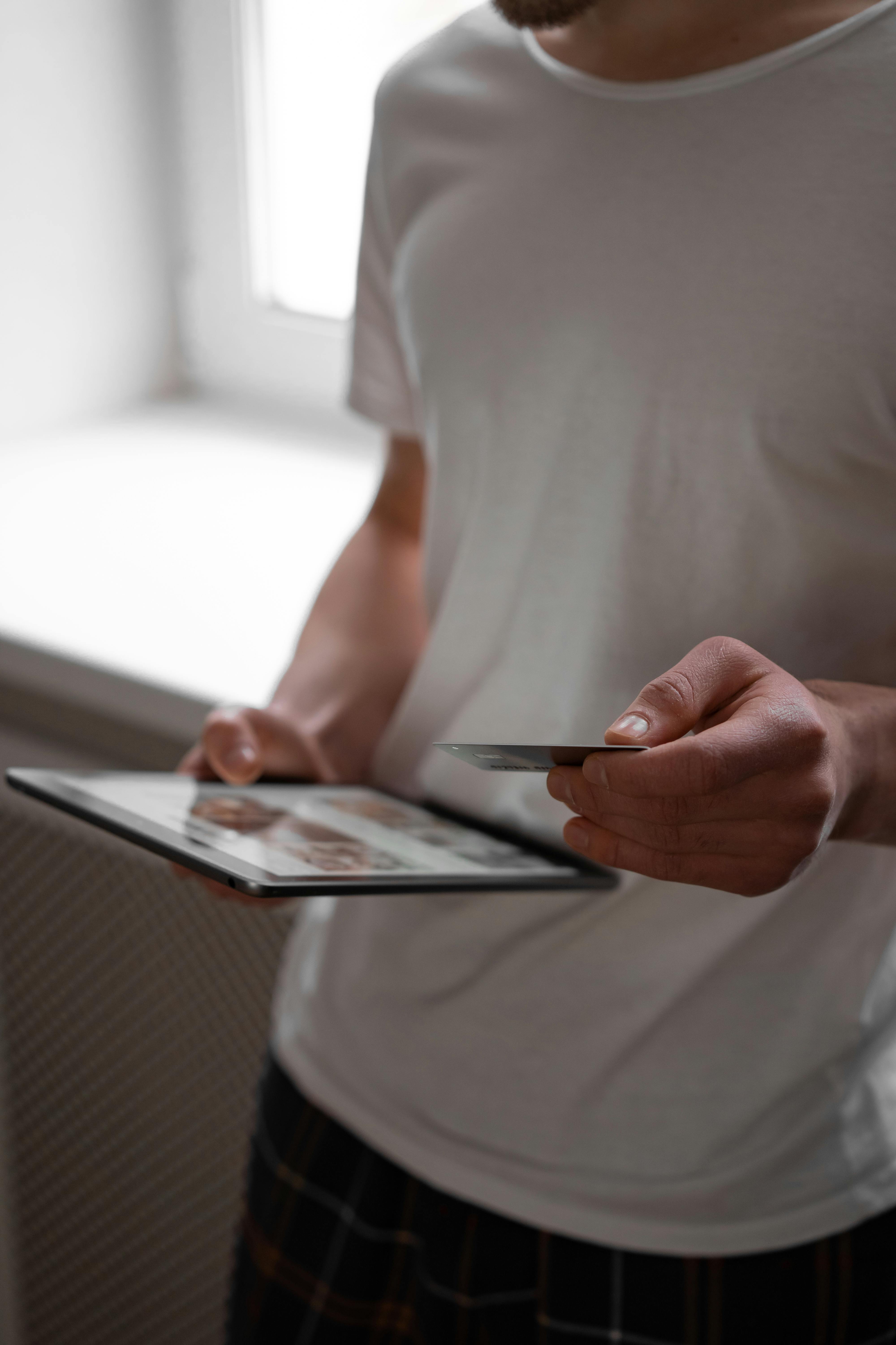 person in white t shirt holding a tablet computer and credit card