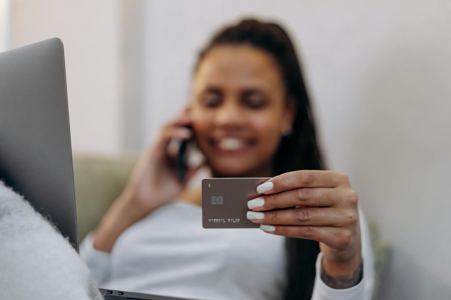 Smiling woman with credit card and smartphone, shopping online at home.