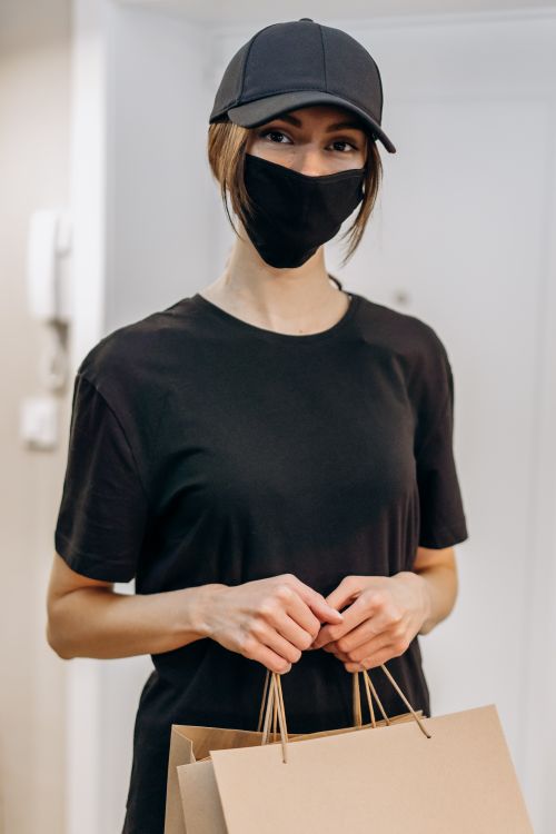 Free A woman wearing a face mask and cap holds shopping bags indoors. Stock Photo