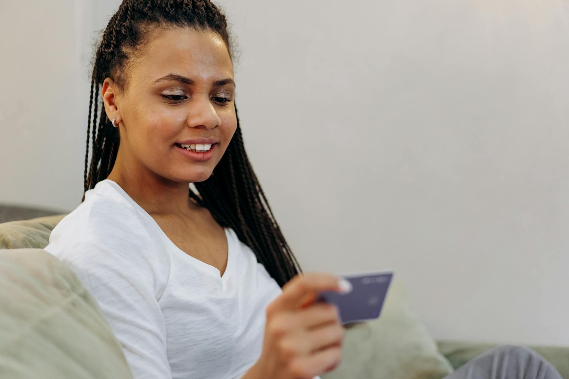 A woman in a white shirt smiling while holding a credit card indoors, showcasing modern banking convenience.