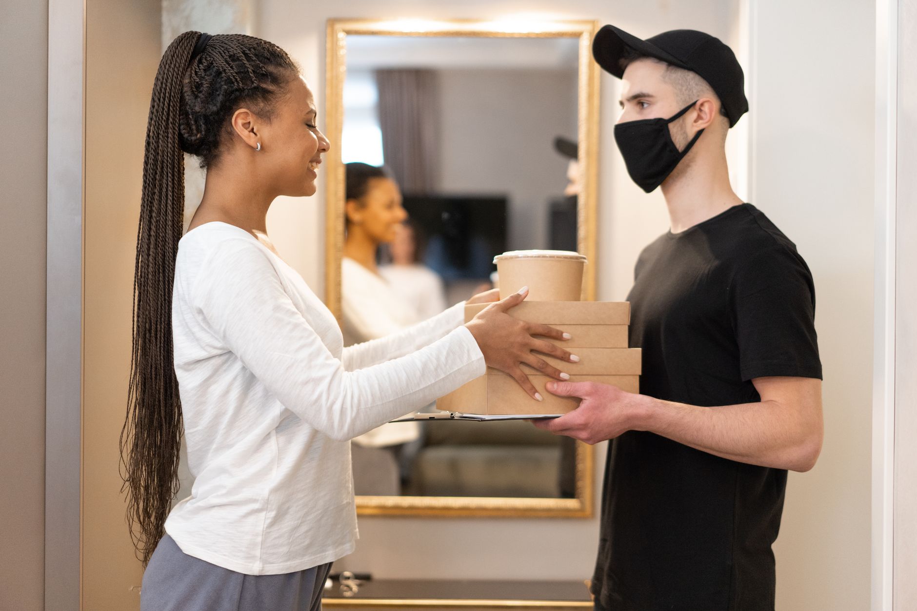 운전면허 적성검사 및 갱신 온라인 신청 가이드: 기간 놓치면 벌금 부과 5 A delivery driver hands packages to a smiling woman indoors, showcasing modern online shopping convenience.