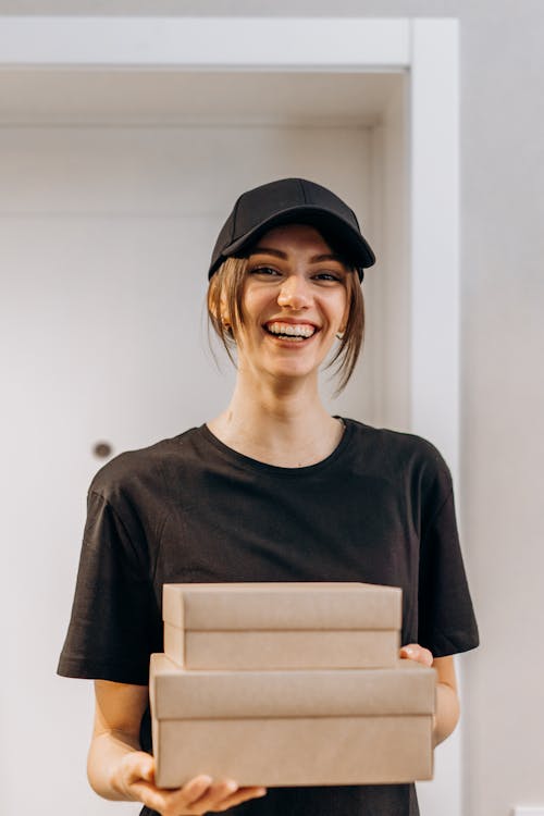 Smiling Woman in Black Crew Neck Shirt Holding Brown Boxes