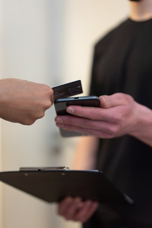 A Man in Black Shirt Holding Black Smartphone to Scan a Credit Card