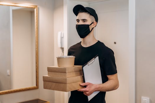 Masked courier delivering food packages during pandemic indoors, representing contactless service.