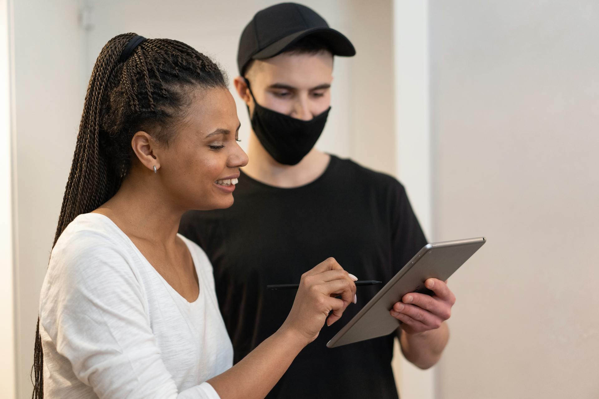 Woman signing for a delivery on a digital tablet held by a masked delivery man indoors.