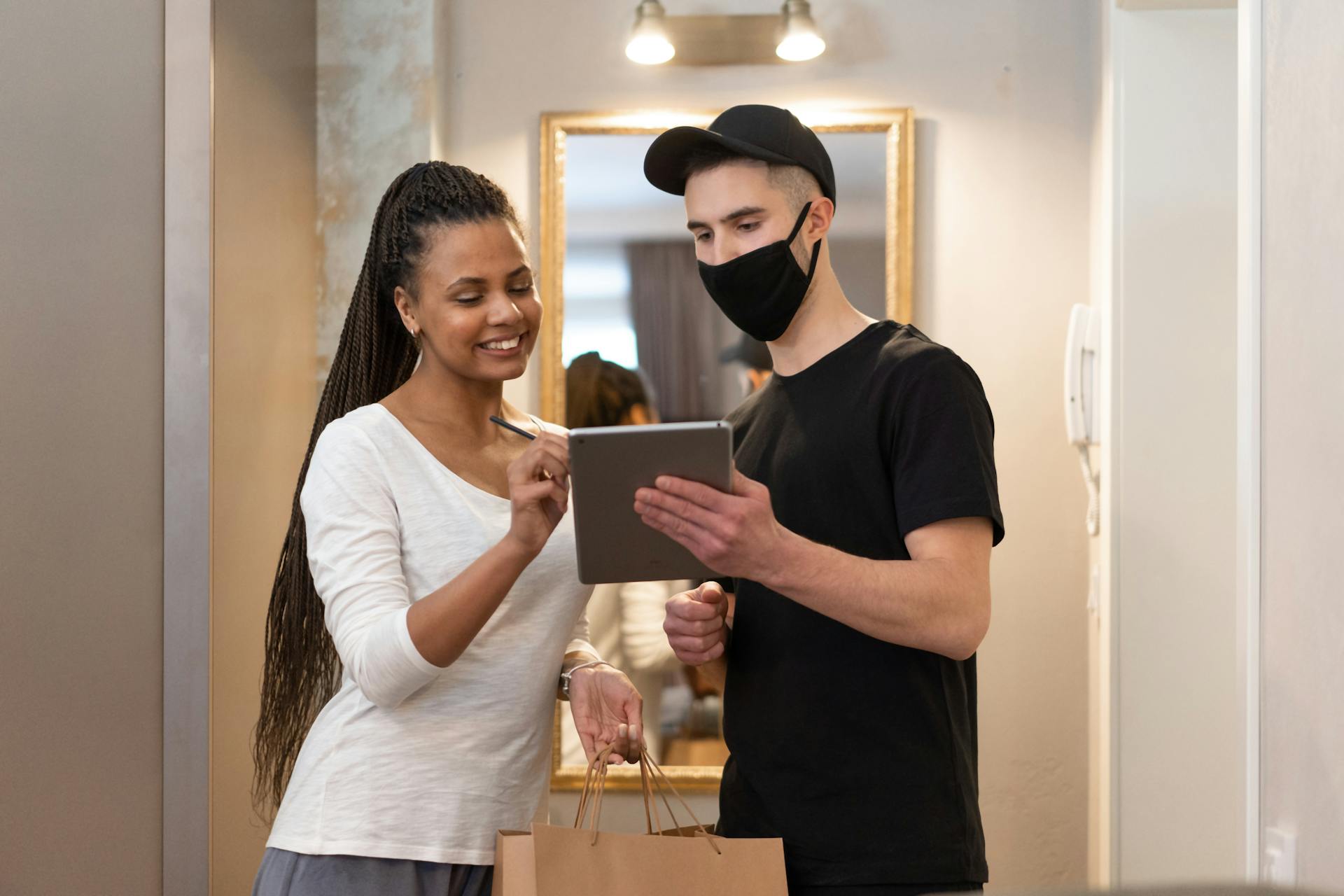 A food delivery scene with a happy customer signing on a digital device indoors.