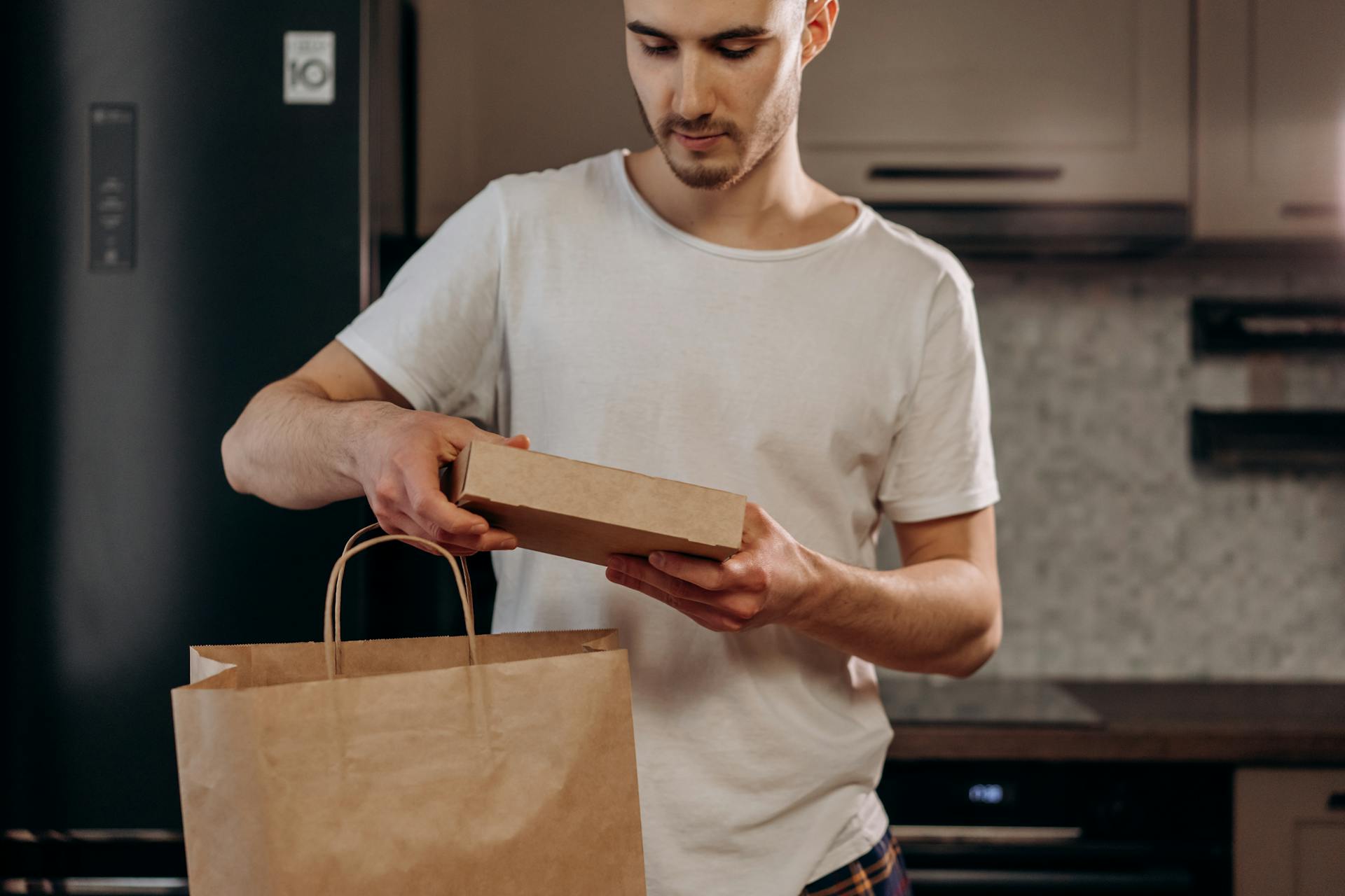 Young man in a modern kitchen unpacking a food delivery package. Ideal for delivery service marketing.