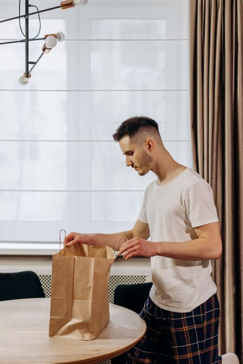 Free A man in casual attire unpacks a delivery bag in a warm and cozy home interior. Stock Photo