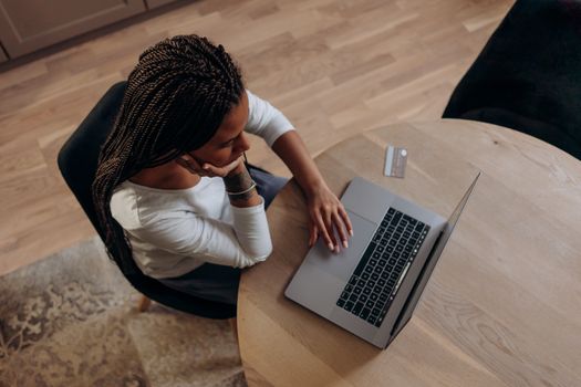 Black woman sitting with a laptop, contemplating an online purchase using a credit card.