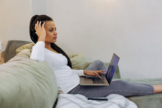 Side view of a woman with braid hairstyle using a laptop on a sofa at home.