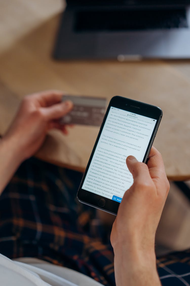 A Person Using His Cellphone And Credit Card For Online Transaction