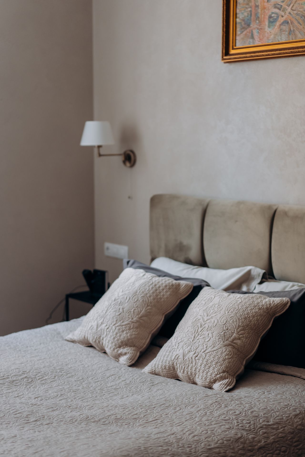 Neutral bedroom with quilted throw pillows arranged against a beige upholstered headboard
