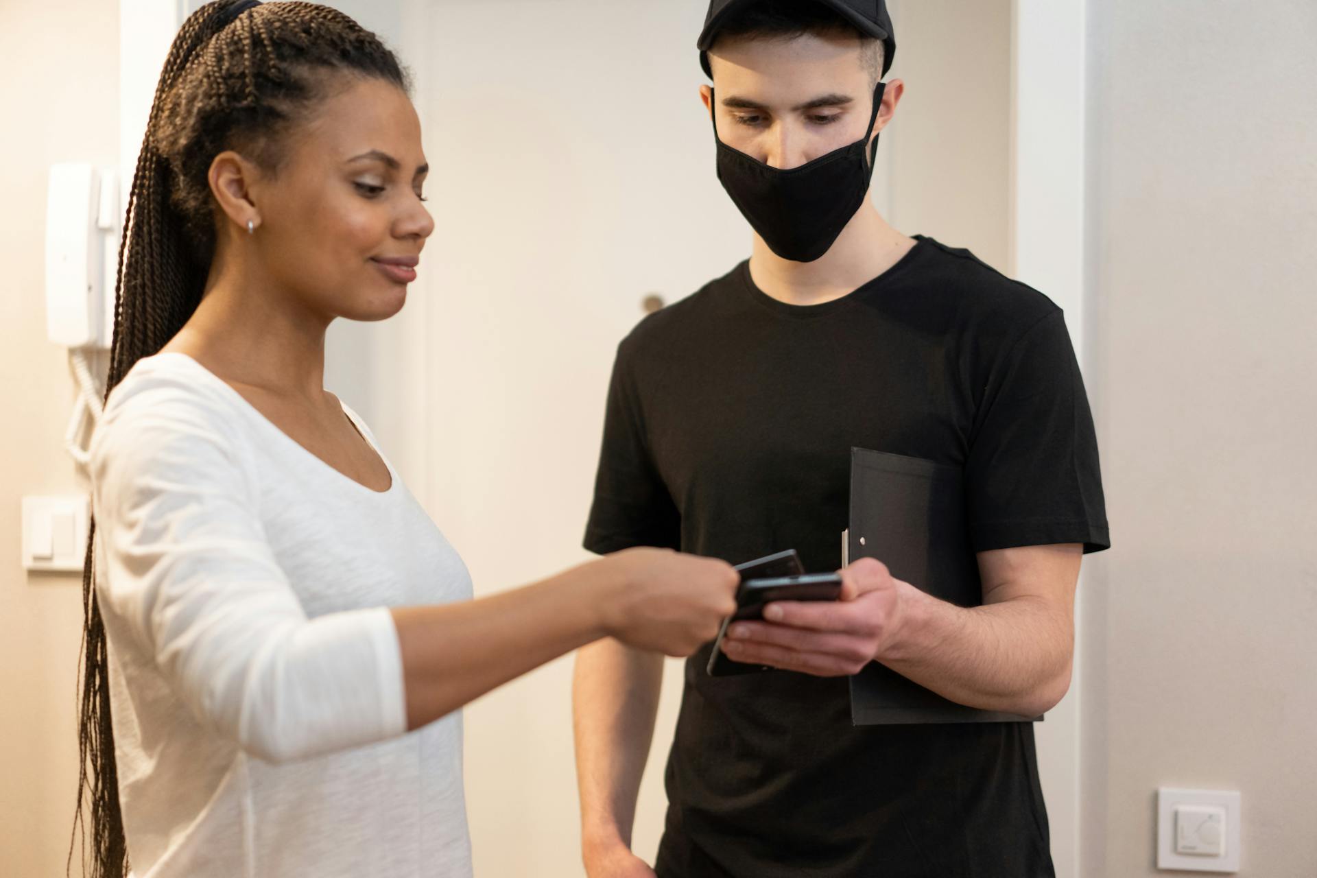 Woman using smartphone for cashless payment with delivery person at home.