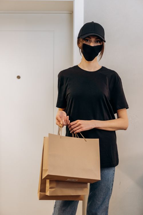 Free A young woman wearing a mask and cap holds shopping bags, representing modern delivery service. Stock Photo