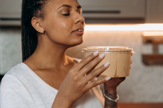 A woman savoring the aroma of a takeaway meal in a cozy kitchen setting.