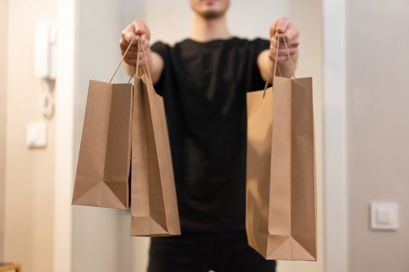 Person holding several kraft paper carrier bags, photo by Mikhail Nilov on Pexels
