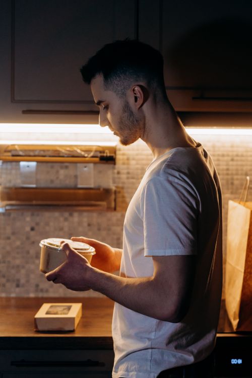 Free Caucasian man examining takeout box in kitchen with under-cabinet lighting. Stock Photo